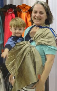 Preschooler with Down Syndrome in gold silk Sakura Bloom sling in front of Sakura Bloom display at JPMA ABC kids show